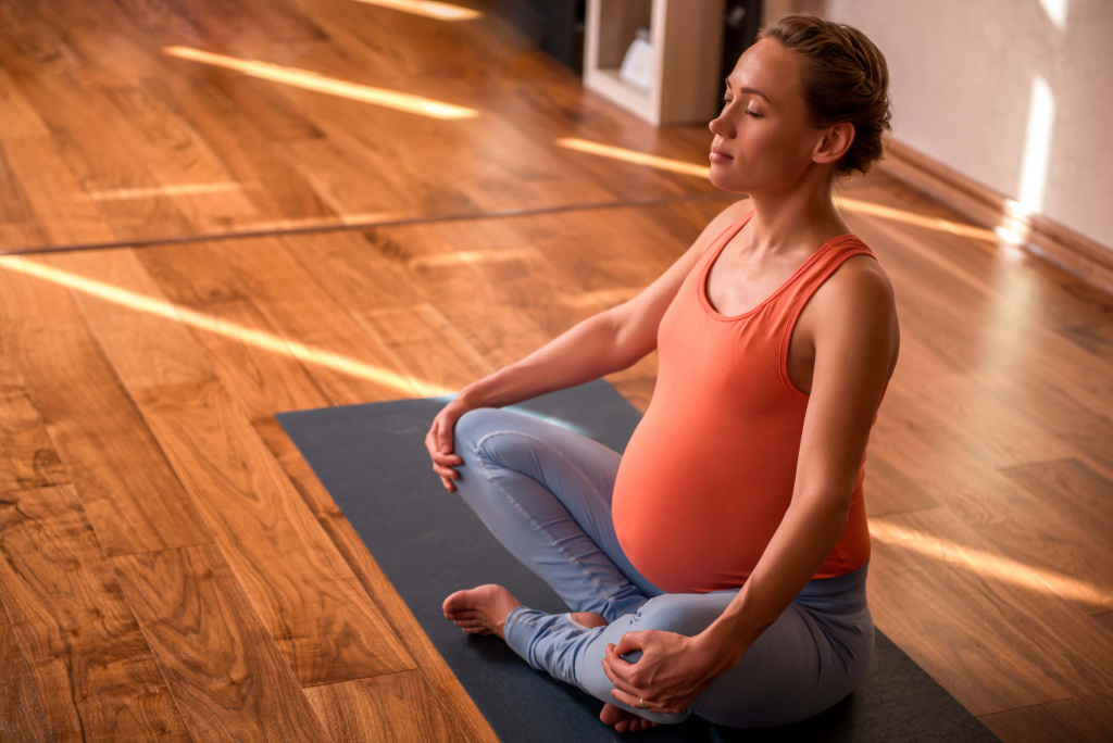 Беременная в оранжевой майке занимается йогой