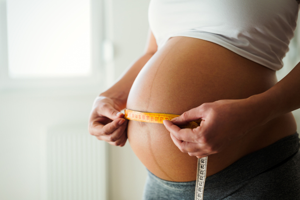 Беременная женщина измеряет размер живота