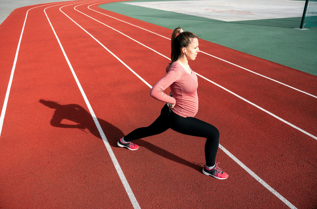 Беременная делает разминку перед бегом на стадионе